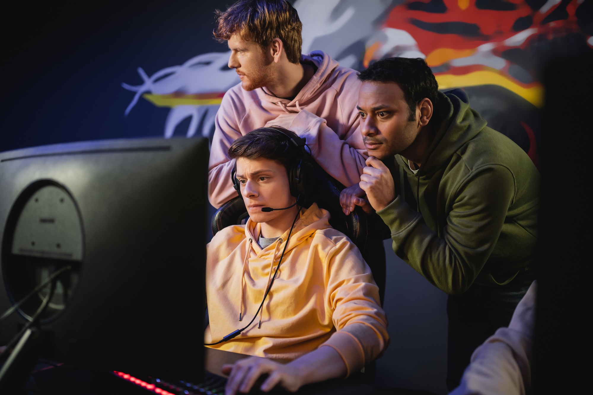 Focused indian man standing near friend playing video game on computer in gaming club